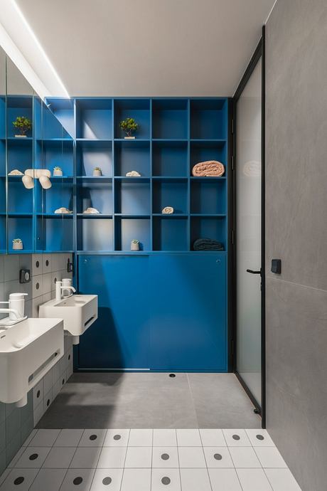 Modern bathroom with blue built-in shelving, white vanity, and geometric tiled floor.