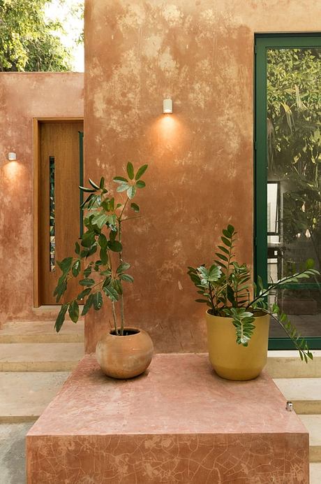 Terracotta exterior with potted plants, recessed lighting, and natural stone bench.