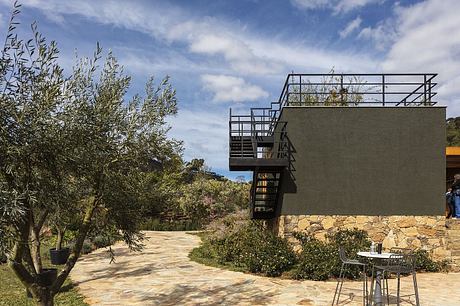 Modern stone and metal building with outdoor seating area and lush landscaping.