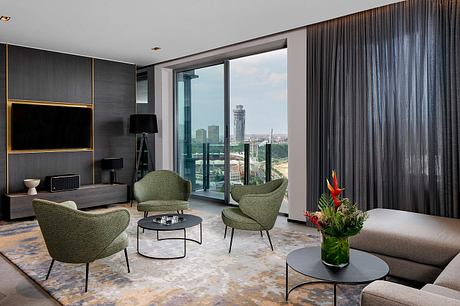 Sleek, modern living room with large windows, plush green chairs, and a cityscape view.