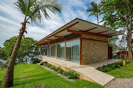 A modern tropical villa with a stone exterior, large windows, and a wooden roof structure.