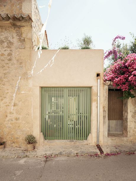 A quaint stone facade with a green slat gate, surrounded by vibrant flowers and foliage.