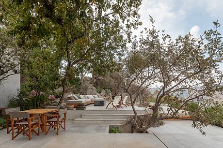 Lush outdoor lounge area with concrete patio, wood furniture, and surrounding greenery.