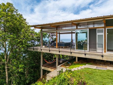 Modern wooden house with large covered deck overlooking lush greenery and ocean view.