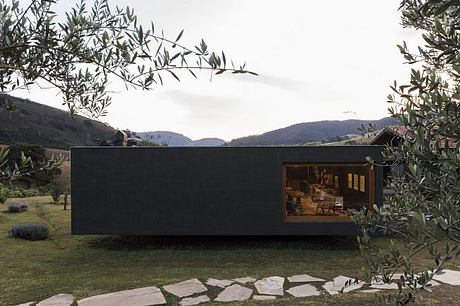 A modern, dark-colored home set amid a lush, mountainous landscape, with large windows providing a scenic view.