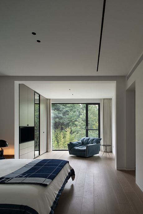 Spacious, modern bedroom with a cozy sitting area and large windows overlooking greenery.