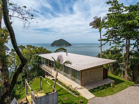 Modern glass house with wooden roof overlooking lush island and ocean.