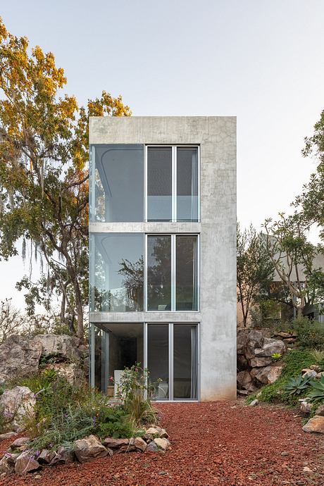 A modern, multi-story concrete structure with large windows surrounded by lush landscaping.