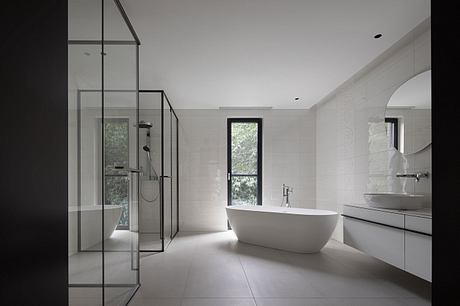 Sleek, modern bathroom with freestanding tub, glass shower, and large window overlooking nature.