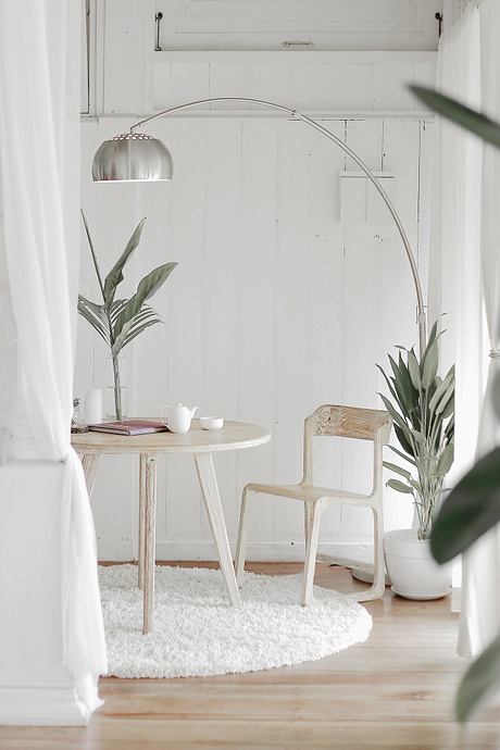 Minimalist room with a round wooden table, arched floor lamp, and lush indoor plants.