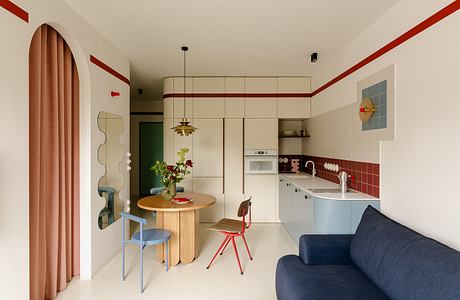 A cozy, modern kitchen with a round wooden table, hanging lamp, and colorful accents.