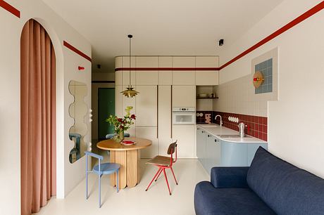 A cozy, modern kitchen with a round wooden table, hanging lamp, and colorful accents.