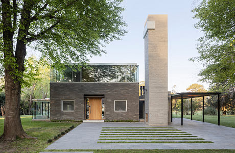 Modern two-story home with glass walls, brick exterior, and tall chimney surrounded by trees.