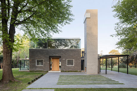 Modern two-story home with glass walls, brick exterior, and tall chimney surrounded by trees.