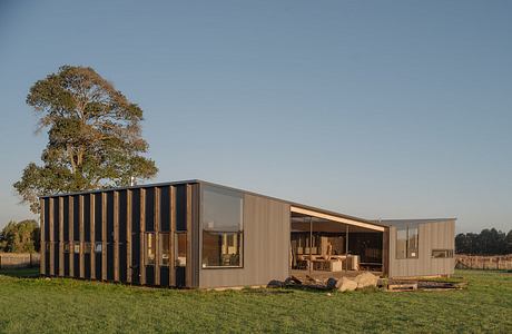 A modern, modular structure with wood and glass facade amidst a grassy field and trees.