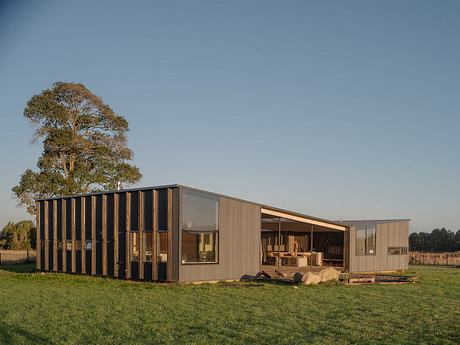 A modern, modular structure with wood and glass facade amidst a grassy field and trees.