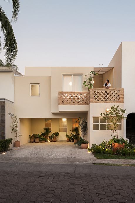 Contemporary adobe-style residential exterior with latticed balconies, potted plants, and paved courtyard.