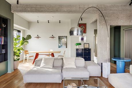 Modern open-plan living space with concrete beams, gray sofa, and industrial lighting.