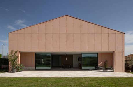 A modern, minimalist structure with large glass windows overlooking a grassy lawn.