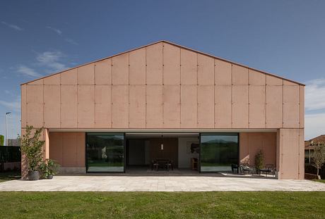 A modern, minimalist structure with large glass windows overlooking a grassy lawn.