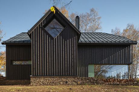 A modern, dark-colored wooden cabin with a triangular roof and large glass windows.