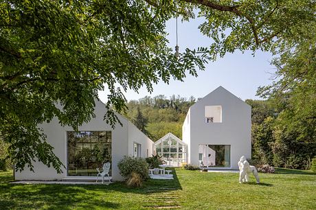 Striking modern white home with glass greenhouse extension and lush garden setting.