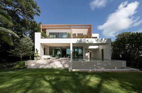 Sleek modern residence with minimalist design, glass walls, and a large pool on lush grounds.