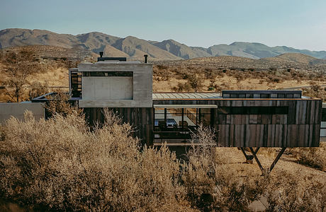 A modern desert residence with concrete and wood construction, nestled amid rugged hills.