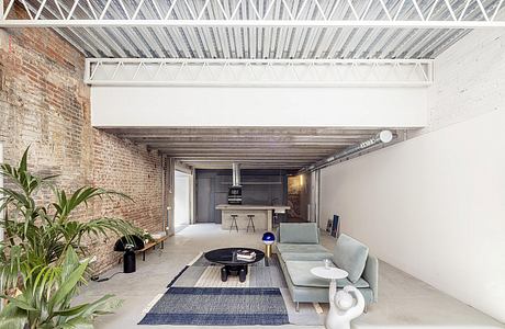 Open-concept living space with exposed brick walls, metal truss ceiling, and modern furnishings.