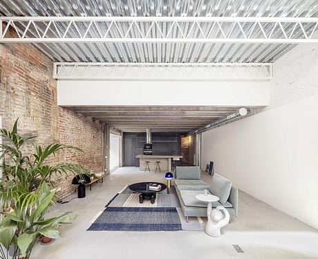 Open-concept living space with exposed brick walls, metal truss ceiling, and modern furnishings.