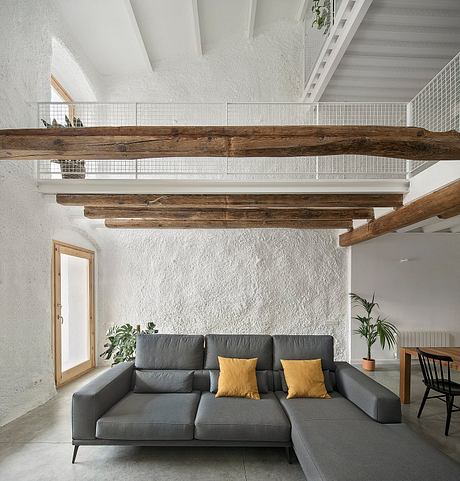 Modern, rustic living room with exposed wood beams, gray sectional, and potted plants.