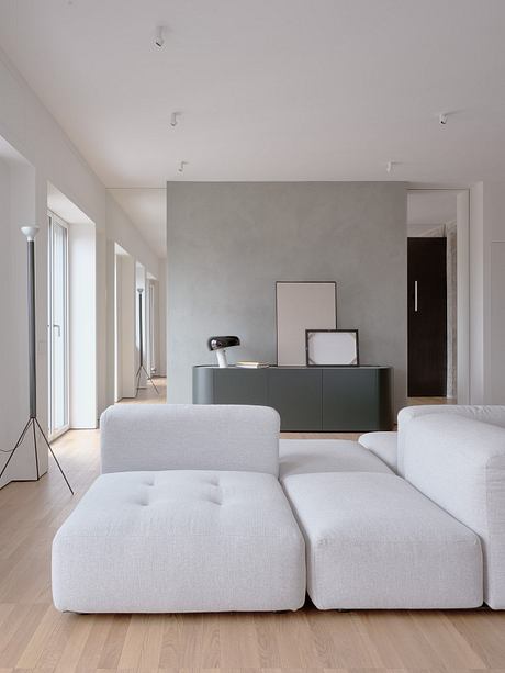 Spacious, minimalist living room with white upholstered furniture, gray storage unit.