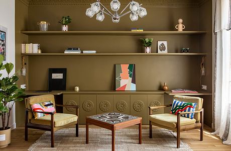 A cozy, eclectic living room with ornate shelving, plush seating, and a striking chandelier.