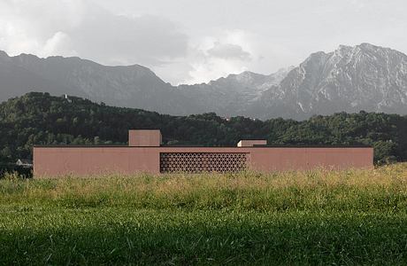 A modern, low-rise building nestled in a mountainous, forested landscape, featuring intricate geometric patterns on its façade.