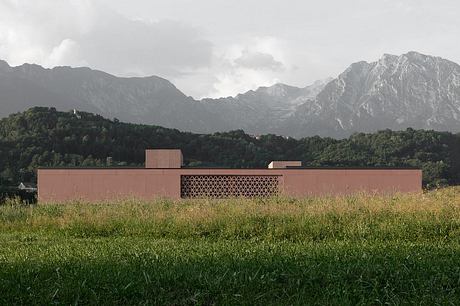 A modern, low-rise building nestled in a mountainous, forested landscape, featuring intricate geometric patterns on its façade.