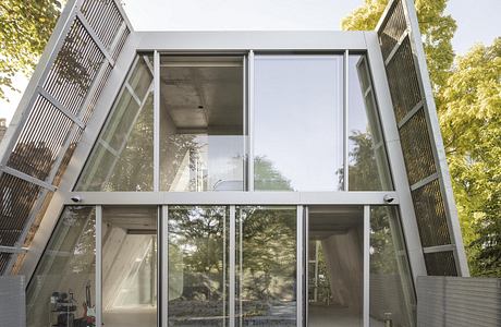 Modern glass pavilion surrounded by lush greenery, featuring angular architectural details.