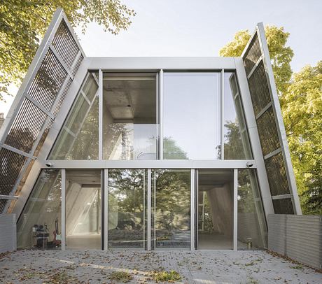 Modern glass pavilion surrounded by lush greenery, featuring angular architectural details.