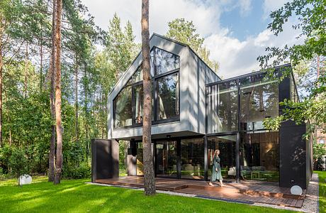 A modern, glass-enclosed forest retreat with a sleek, angular design and a lush, natural backdrop.