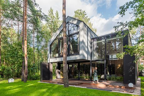 A modern, glass-enclosed forest retreat with a sleek, angular design and a lush, natural backdrop.