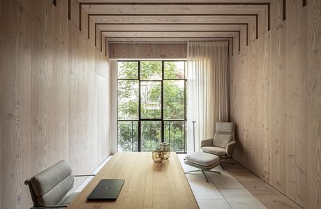 A minimalist, wood-paneled room with a large window overlooking a lush, green outdoor scene.