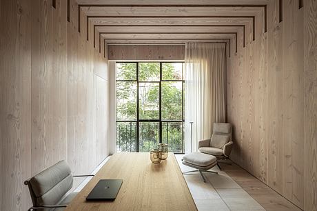 A minimalist, wood-paneled room with a large window overlooking a lush, green outdoor scene.