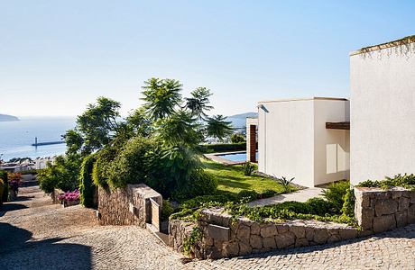 Modern Mediterranean villa with stone walls, lush greenery, and a swimming pool overlooking the sea.