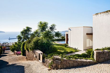 Modern Mediterranean villa with stone walls, lush greenery, and a swimming pool overlooking the sea.