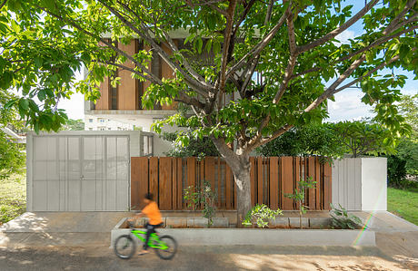 A modern, wood-and-glass residential building with a lush, leafy tree in the foreground.