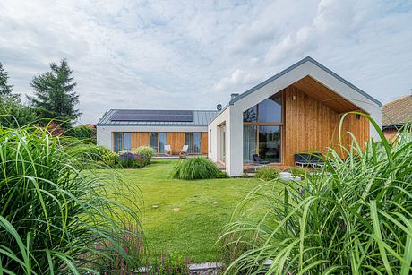 A modern, energy-efficient home with a wooden exterior, solar panels, and a lush, landscaped garden.