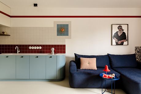 A modern kitchen with retro-style tiles, a blue sofa, and a framed artwork in the living area.