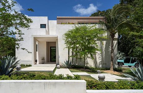 A modern, minimalist home with a welcoming entrance, surrounded by lush tropical foliage.