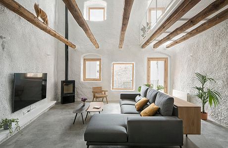 A spacious living room with exposed wooden beams, minimalist furniture, and large windows.