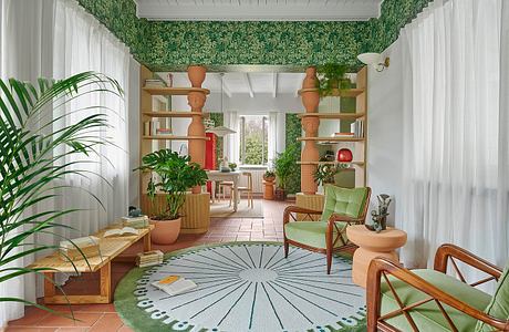 A cozy, plant-filled indoor space with natural wood furnishings and a patterned area rug.