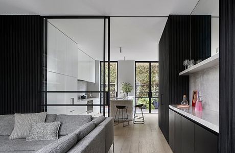 Sleek, modern interior with black accents, floor-to-ceiling windows, and a kitchen visible in the background.